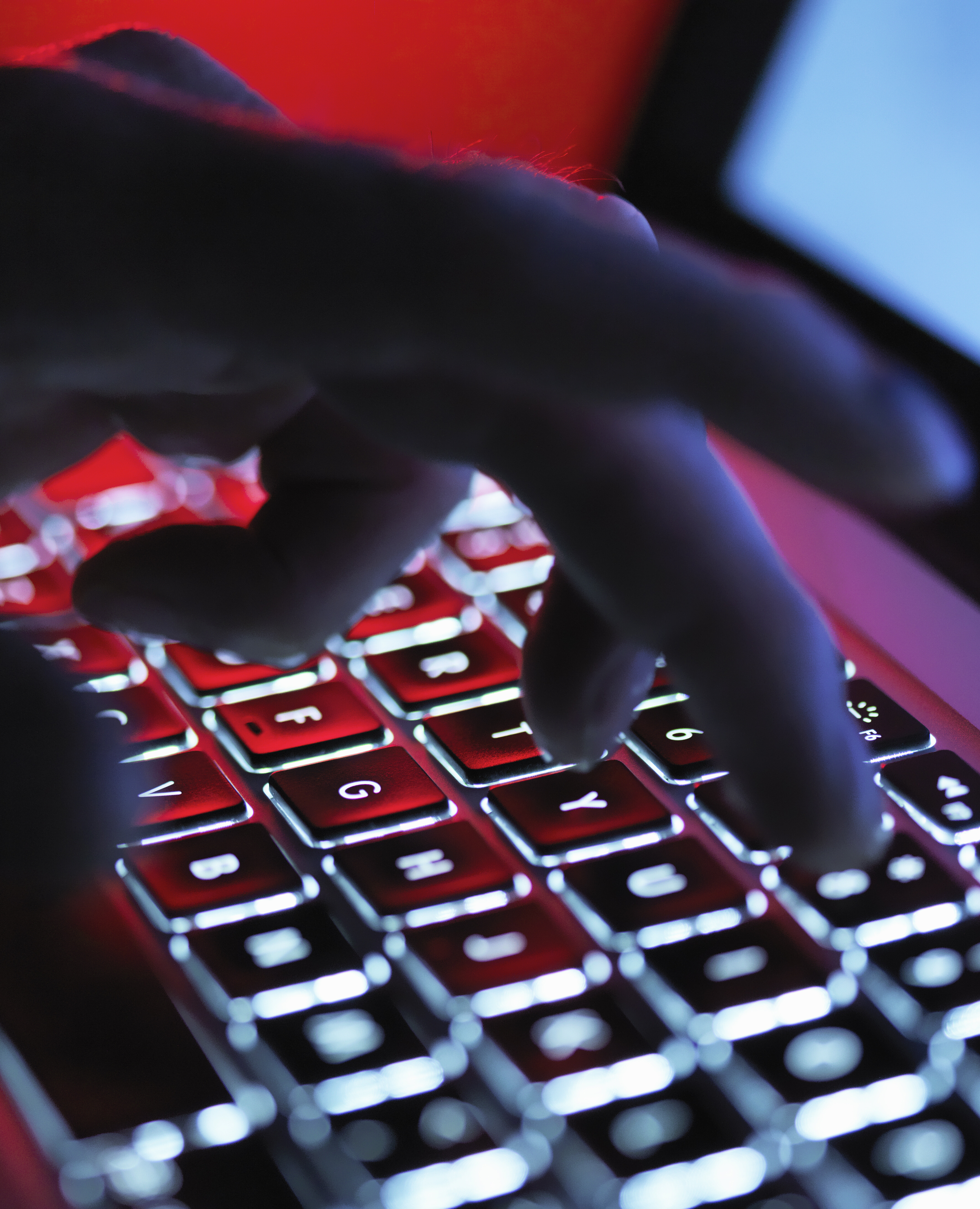 Close up photo of a hand hovering over an illuminated computer keyboard