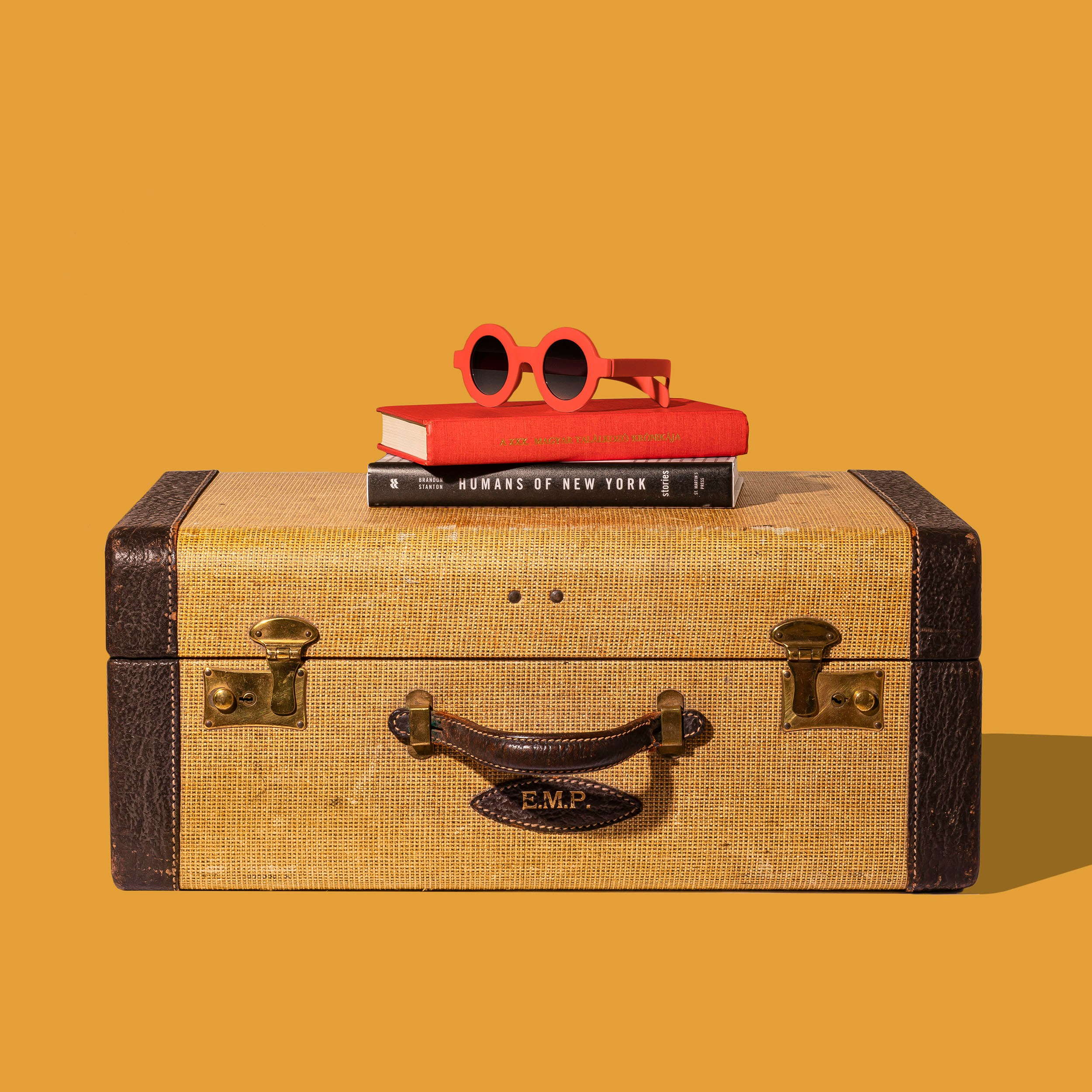 suitcase with two books, and a pair of sunglasses on top