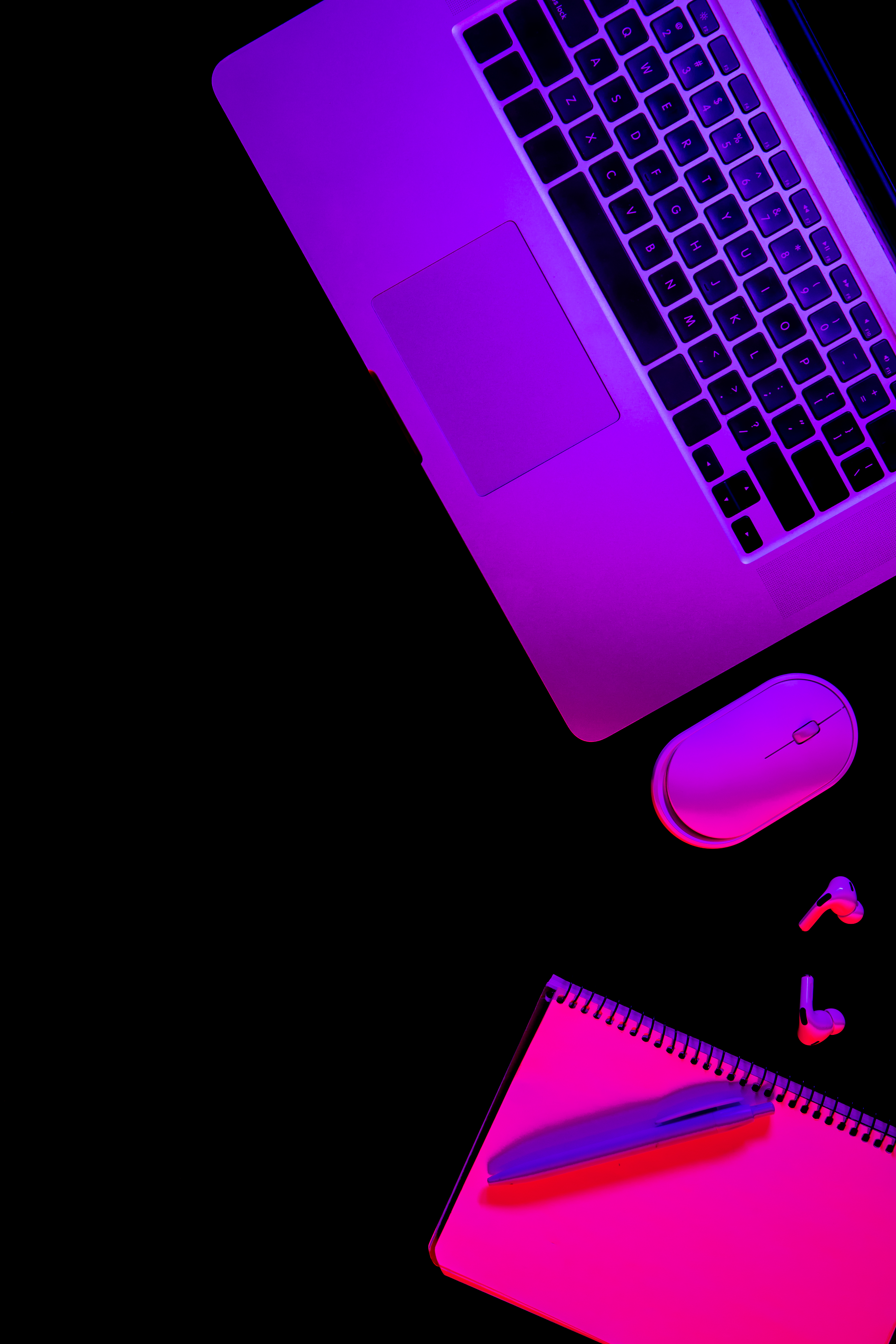 Flat desk layout with open laptop, mouse and notebook with a neon colour wash
